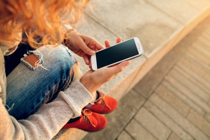Kvinna sitter i fönstret och tittar på telefonen.